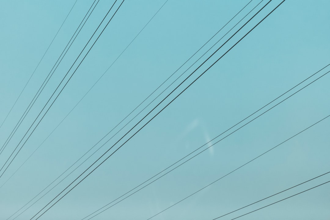 A complex tangle of black electrical wires crossing in a chaotic pattern against a clear blue sky, symbolizing the confusion of an unregulated neighborhood.