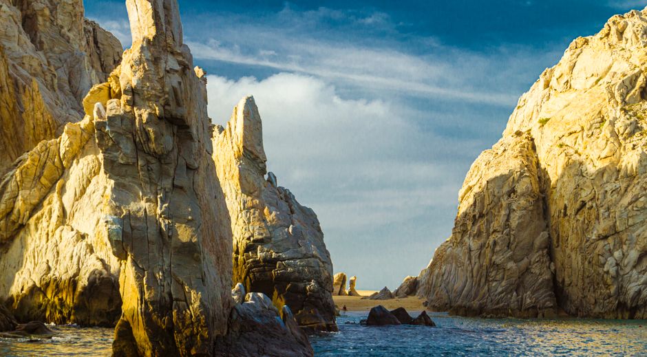 The iconic El Arco rock formation in Cabo San Lucas, Mexico, viewed from the water during a vibrant, golden sunset.