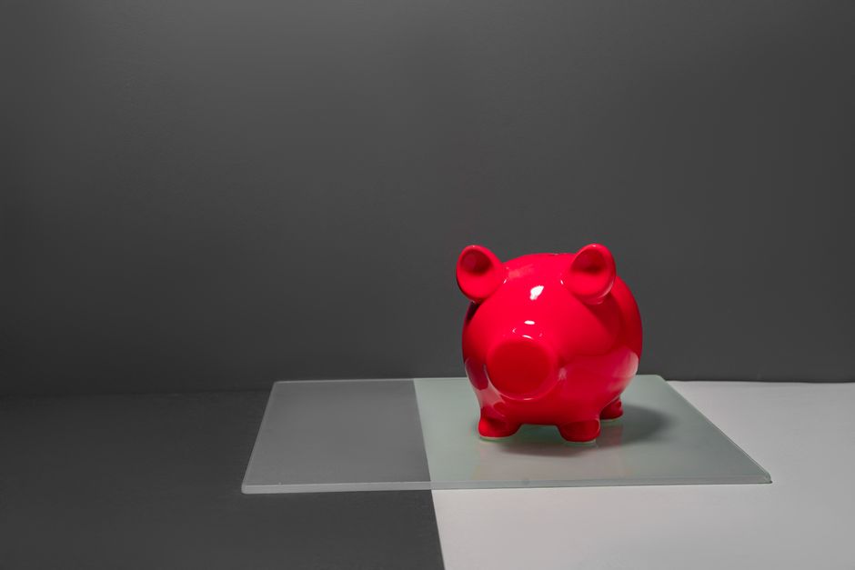 A minimalist photo of a simple house key placed next to a piggy bank on a clean surface, illustrating the concept of savings and the changing cost of real estate services.